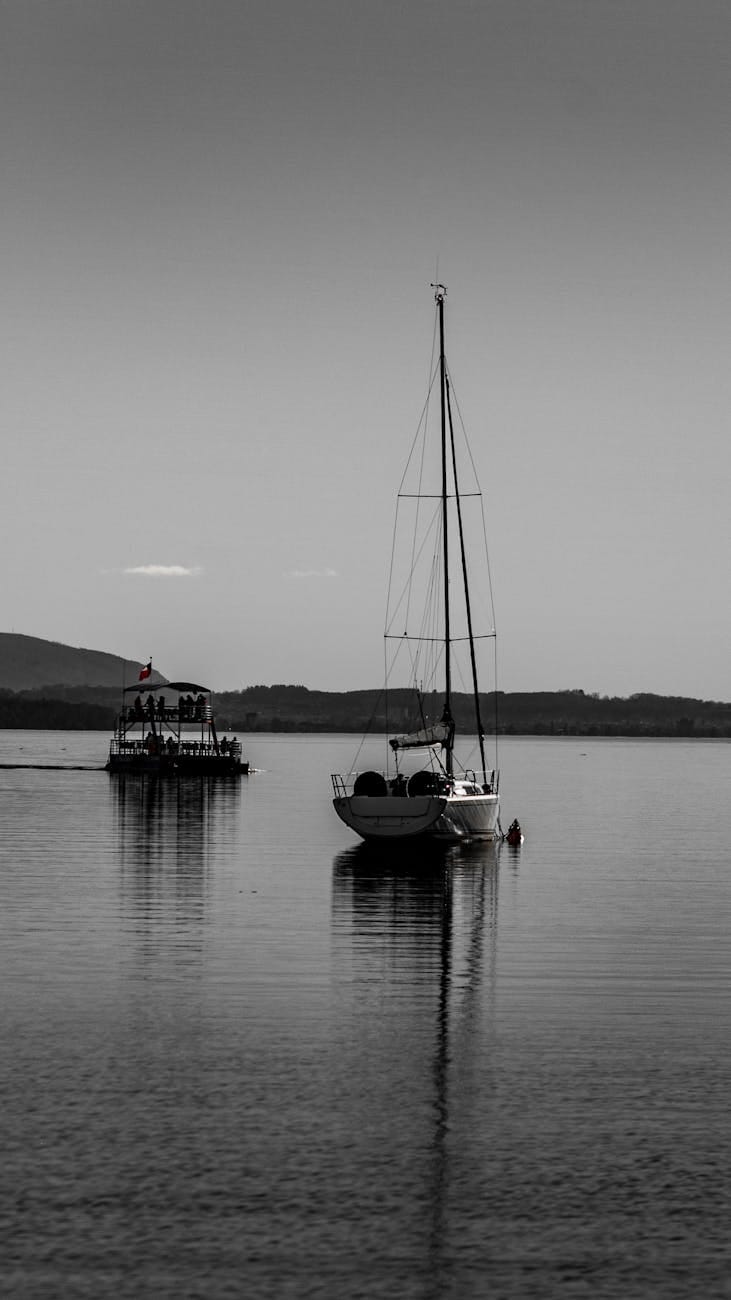 sailboat and vessel on sea coast in black and white